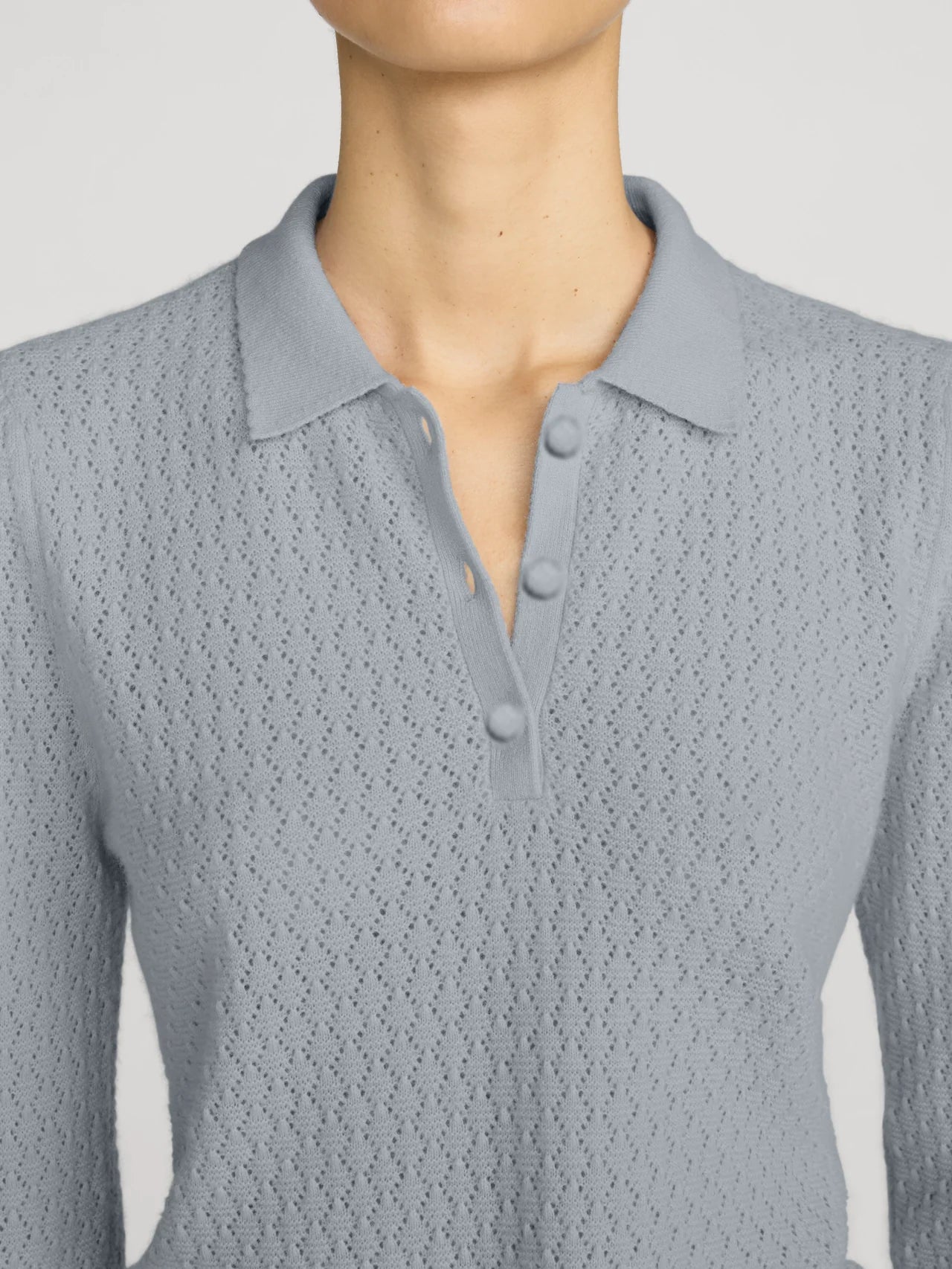 A close-up of a model wearing a light gray textured knit polo shirt with a three-button placket.