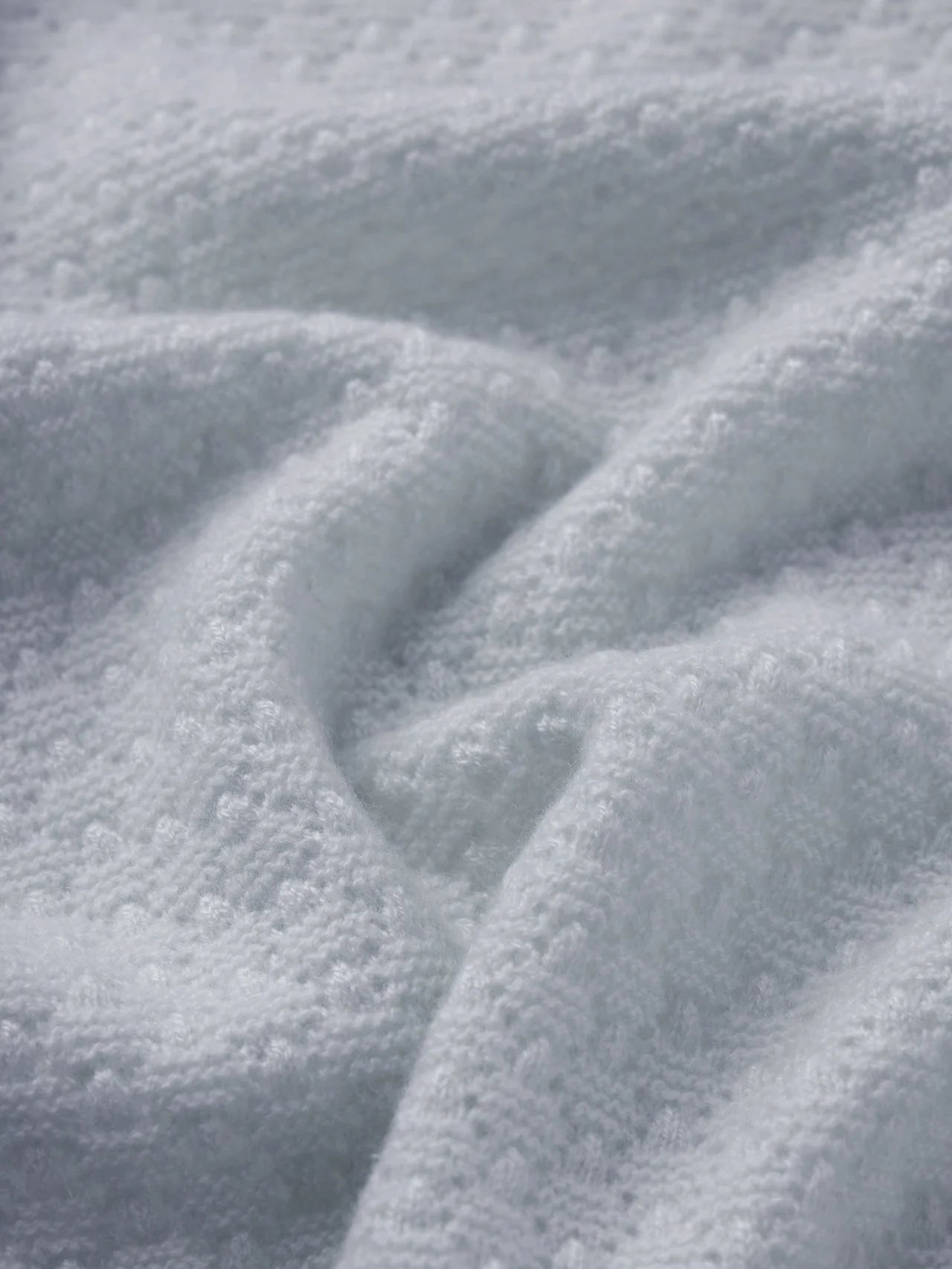 A close-up of a soft, textured white fabric with a plush, looped terry surface and gentle folds.