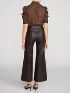 A model shown from the back wearing a brown and black leopard-print short-sleeve blouse with ruffled shoulders and dark brown wide-leg faux-leather pants, paired with black heels, against a light gray studio background.