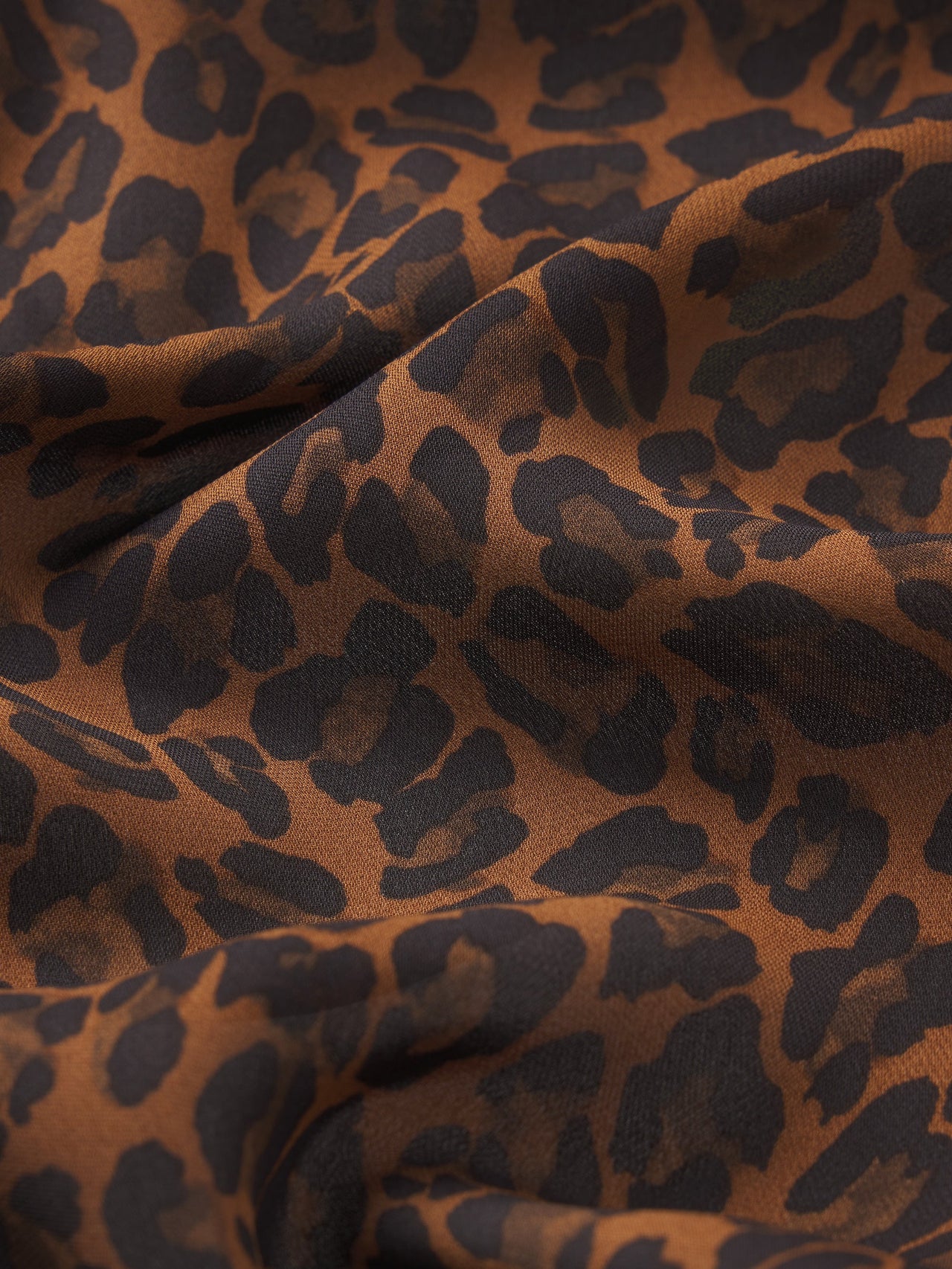 A close-up of draped leopard print fabric with a warm brown base and dark charcoal spots.