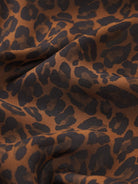 A close-up of draped leopard print fabric with a warm brown base and dark charcoal spots.