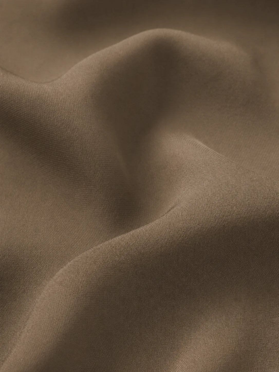 A close-up of draped taupe-brown fabric with soft folds and a smooth matte texture.