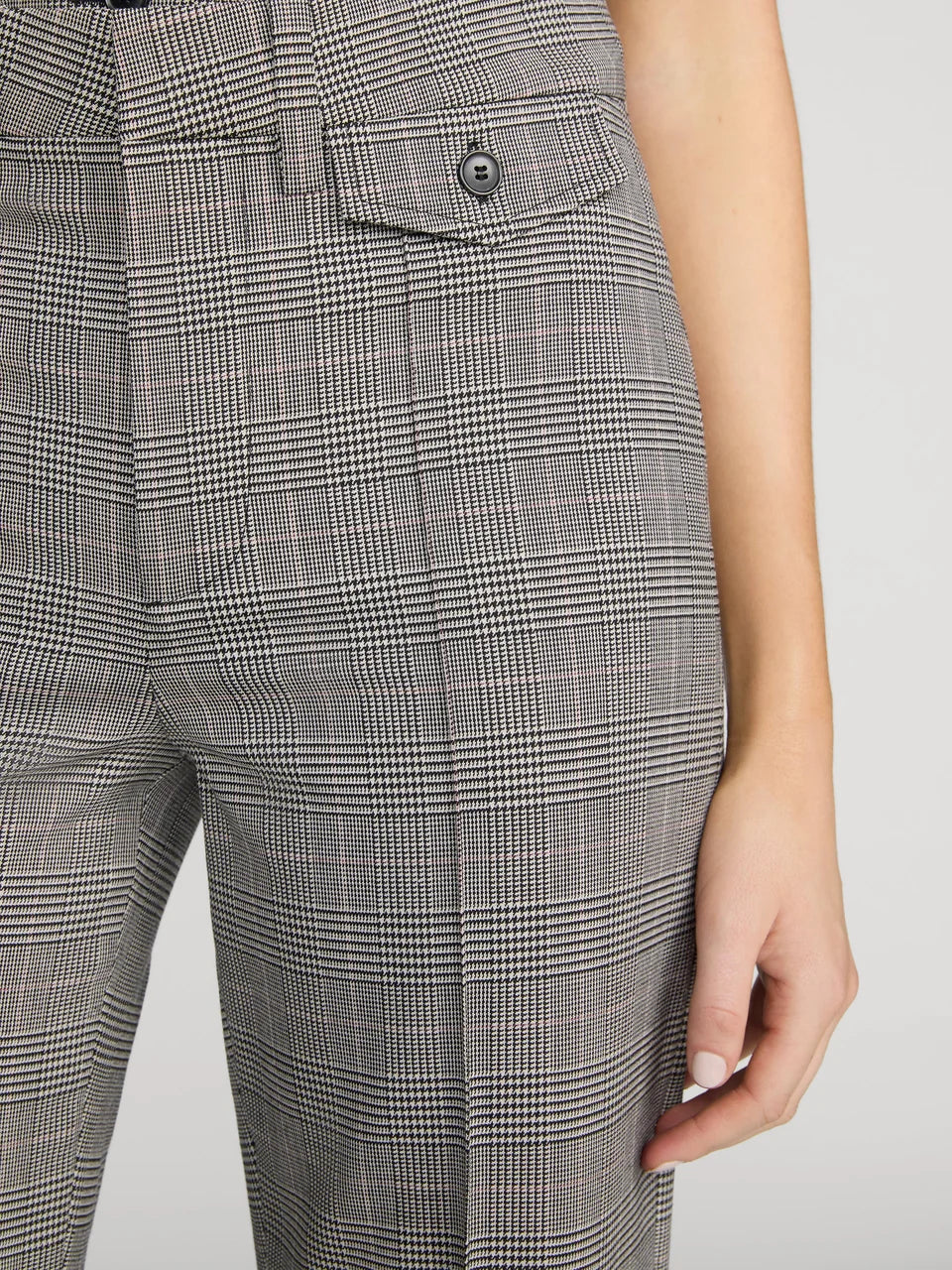 Close-up of a person wearing gray plaid trousers with a buttoned flap pocket and visible hand.