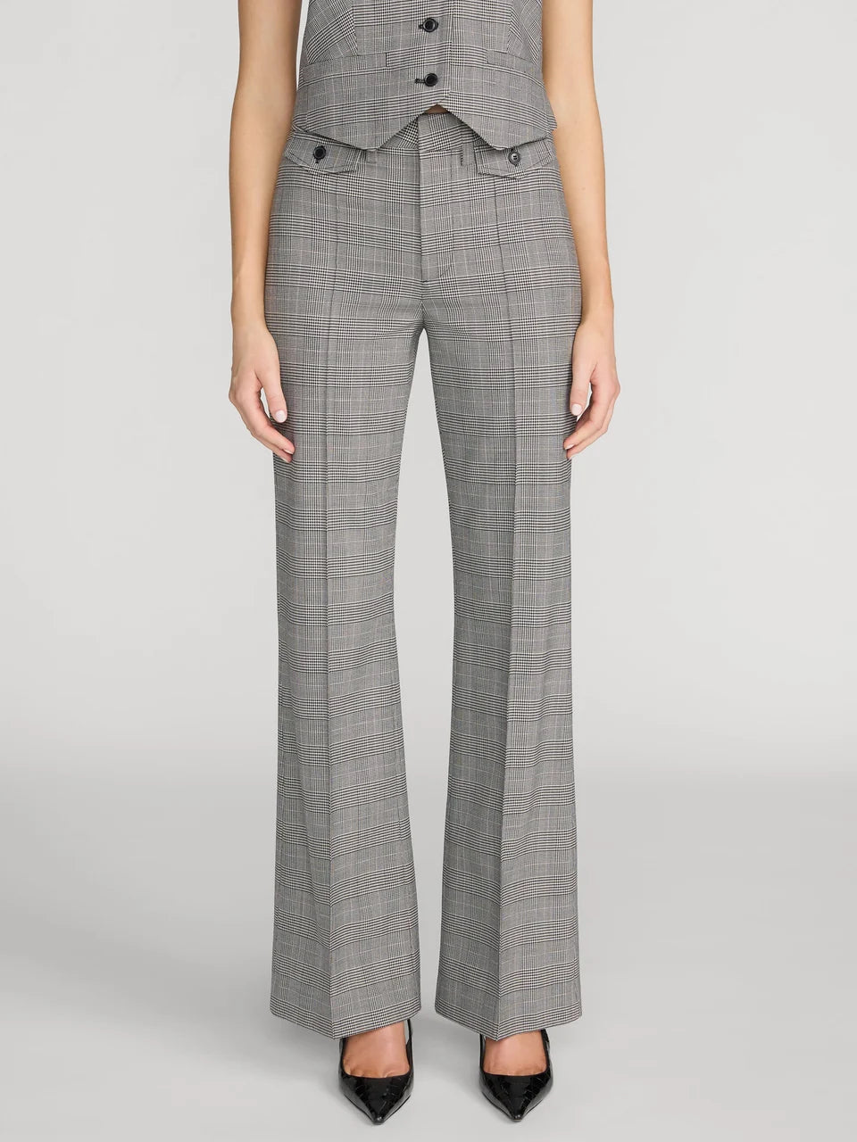 A model wearing a pair of high-waisted, wide-leg gray plaid trousers with a matching vest and black pointed-toe heels, shown against a light gray studio background.