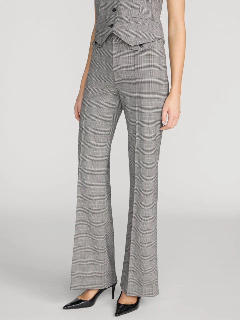 A model is shown from the waist down wearing a gray and white plaid vest and matching wide-leg trousers with black pointed-toe heels, set against a plain light gray studio background.