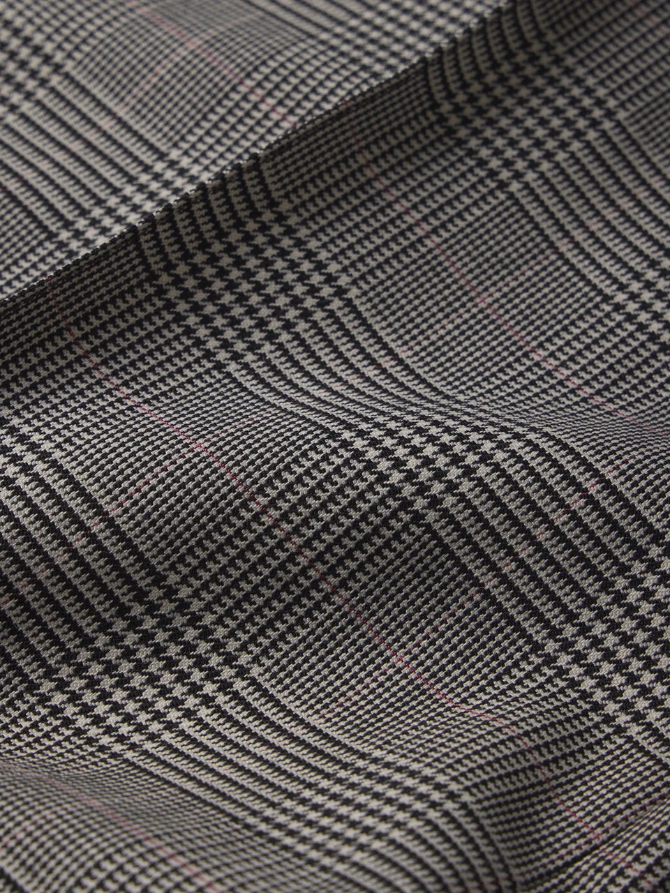 A close-up of a dark gray and black houndstooth fabric with subtle pink and white thread accents, showing the detailed woven texture and soft folds.