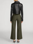 A model shown from the back wearing a black cropped leather jacket and olive green wide-leg trousers, paired with black high-heeled sandals, against a light gray studio background.