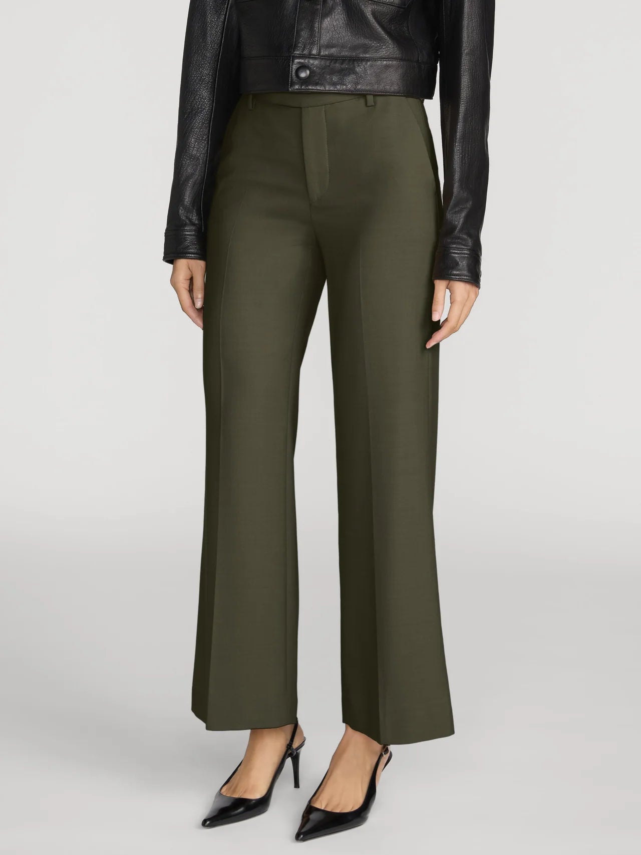 A model wearing olive green wide-leg cropped trousers, styled with a black leather jacket and black pointed-toe heels, against a light gray studio background.