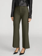 A model wearing olive green wide-leg cropped trousers, styled with a black leather jacket and black pointed-toe heels, against a light gray studio background.