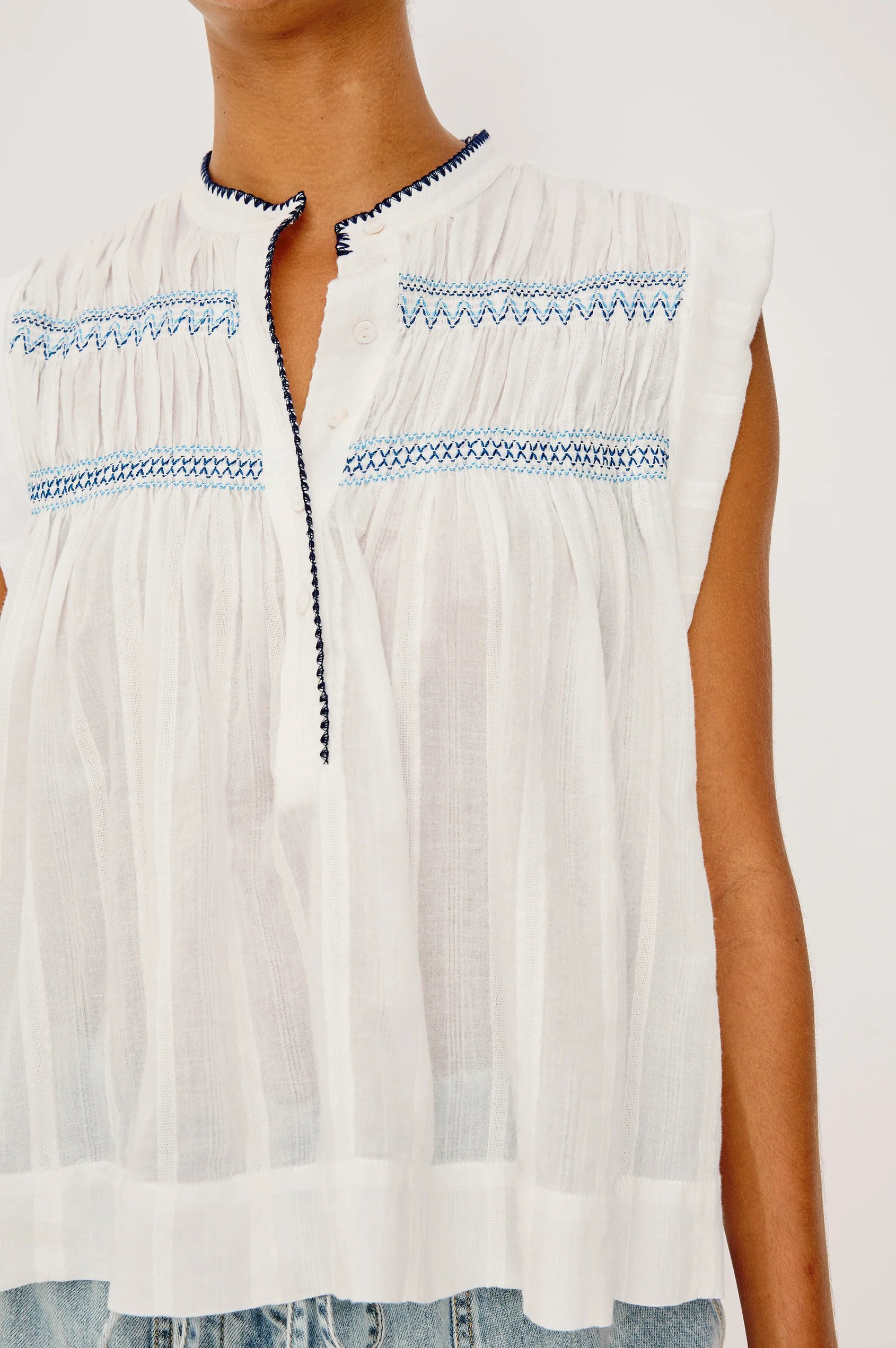 White sleeveless top with blue embroidery on a white background