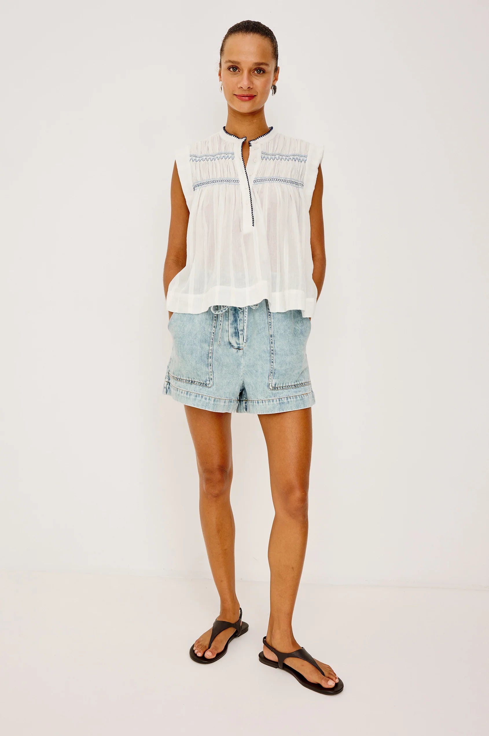 Woman wearing a white sleeveless top and light blue denim shorts on a plain background