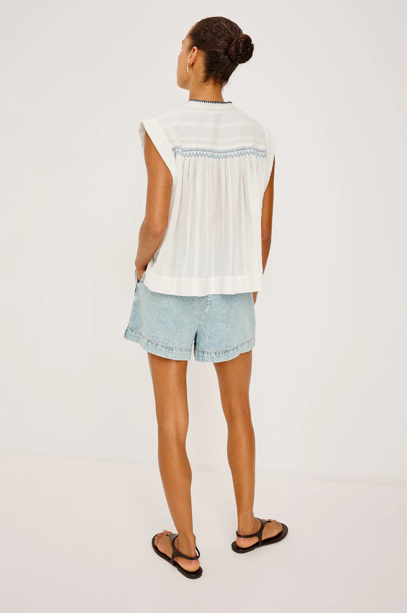 Woman wearing a white sleeveless top and light blue denim shorts on a plain background