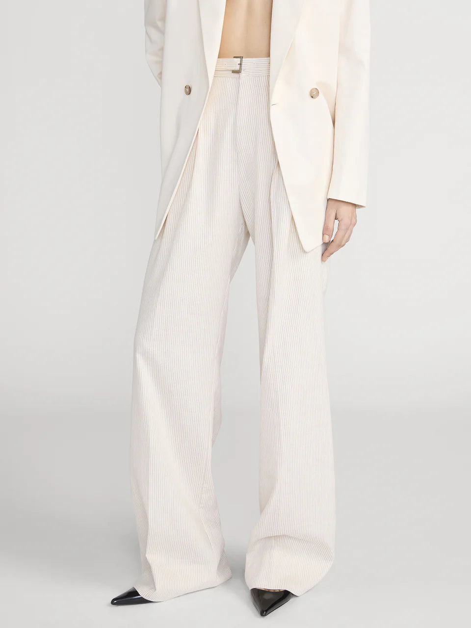 Person wearing a white suit with wide-leg pants on a light gray background