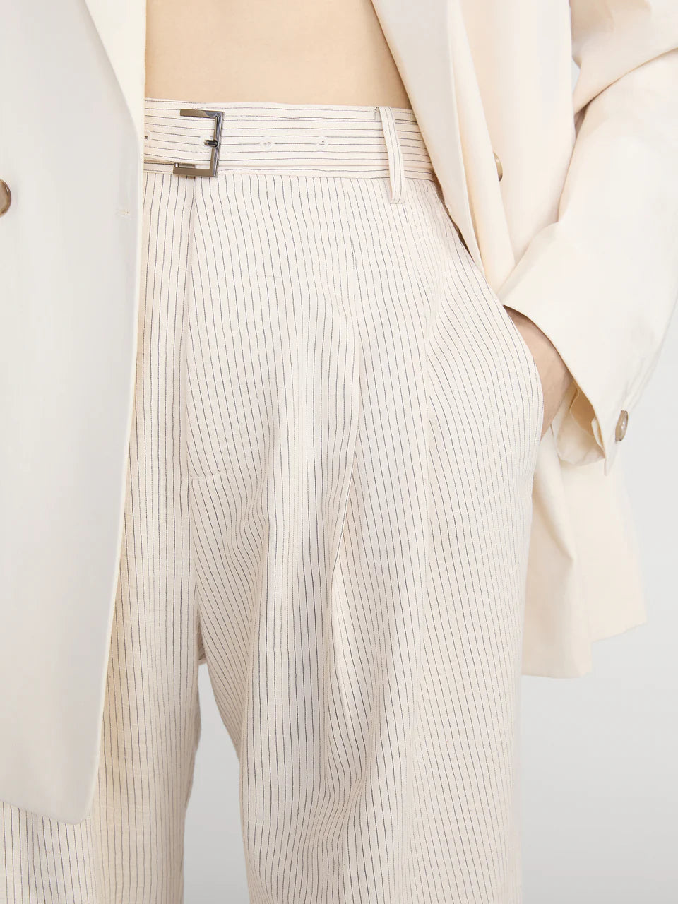 Close-up of a person wearing beige pleated pants with a belt.