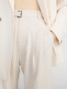 Close-up of a person wearing beige pleated pants with a belt.