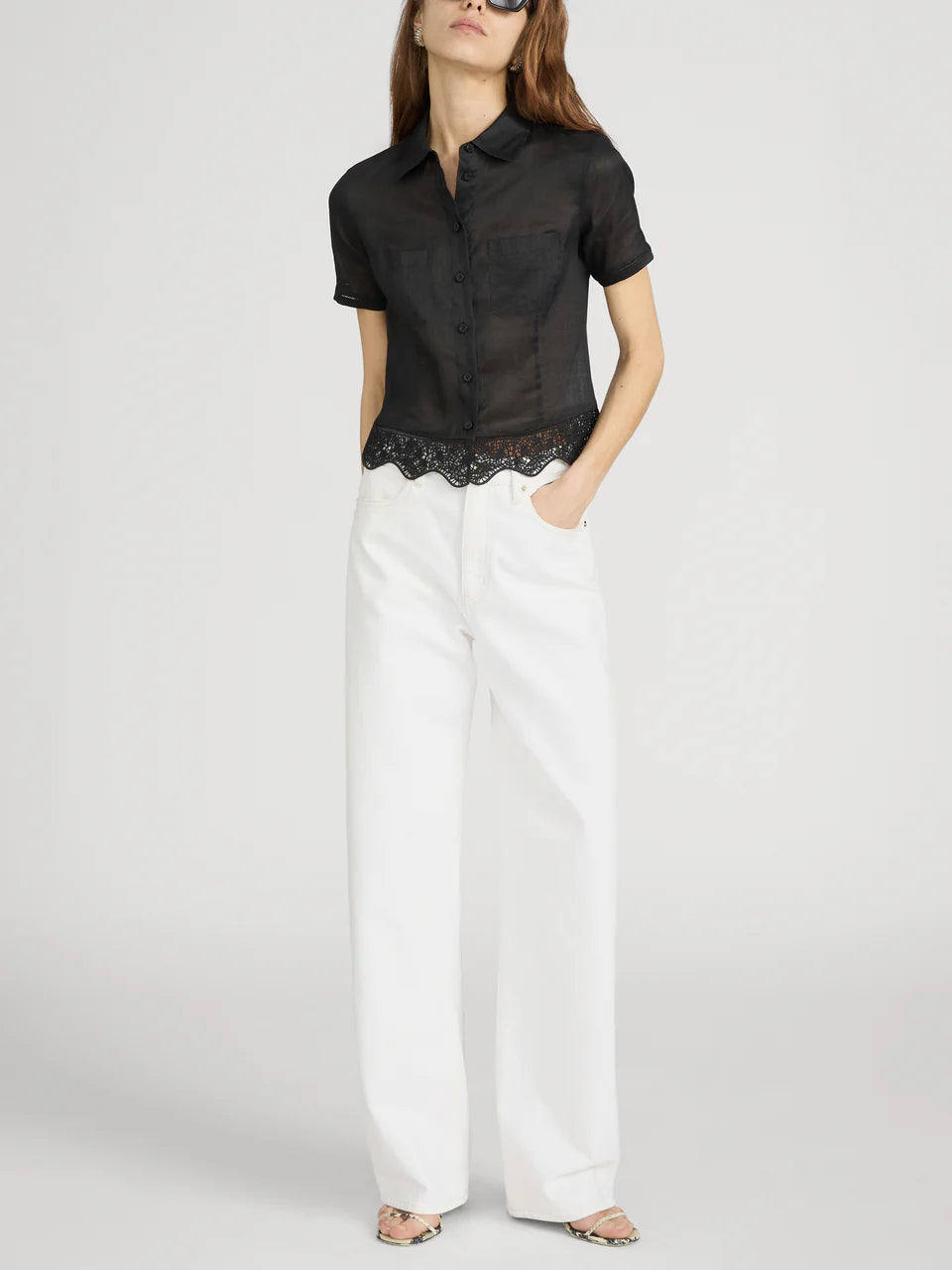 Woman wearing a black shirt with lace trim and white pants on a plain background