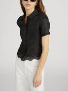 Woman wearing a black short-sleeve blouse with lace trim on a white background
