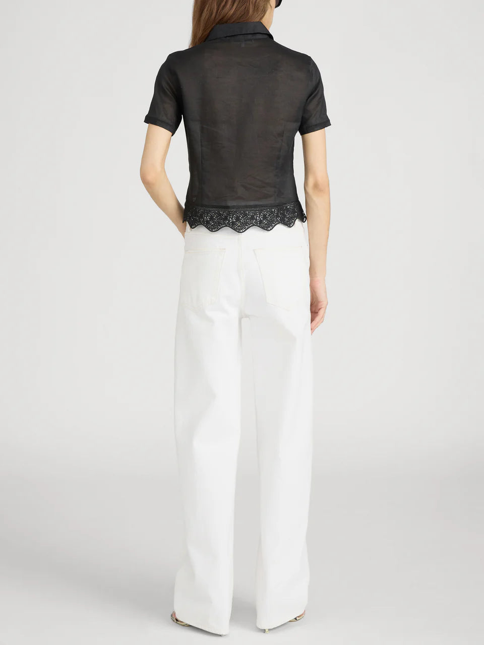 Person wearing a black top with lace trim and white pants on a light gray background