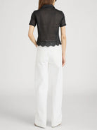 Person wearing a black top with lace trim and white pants on a light gray background