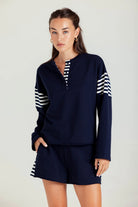 Woman wearing a navy outfit with white and black striped sleeves on a plain background