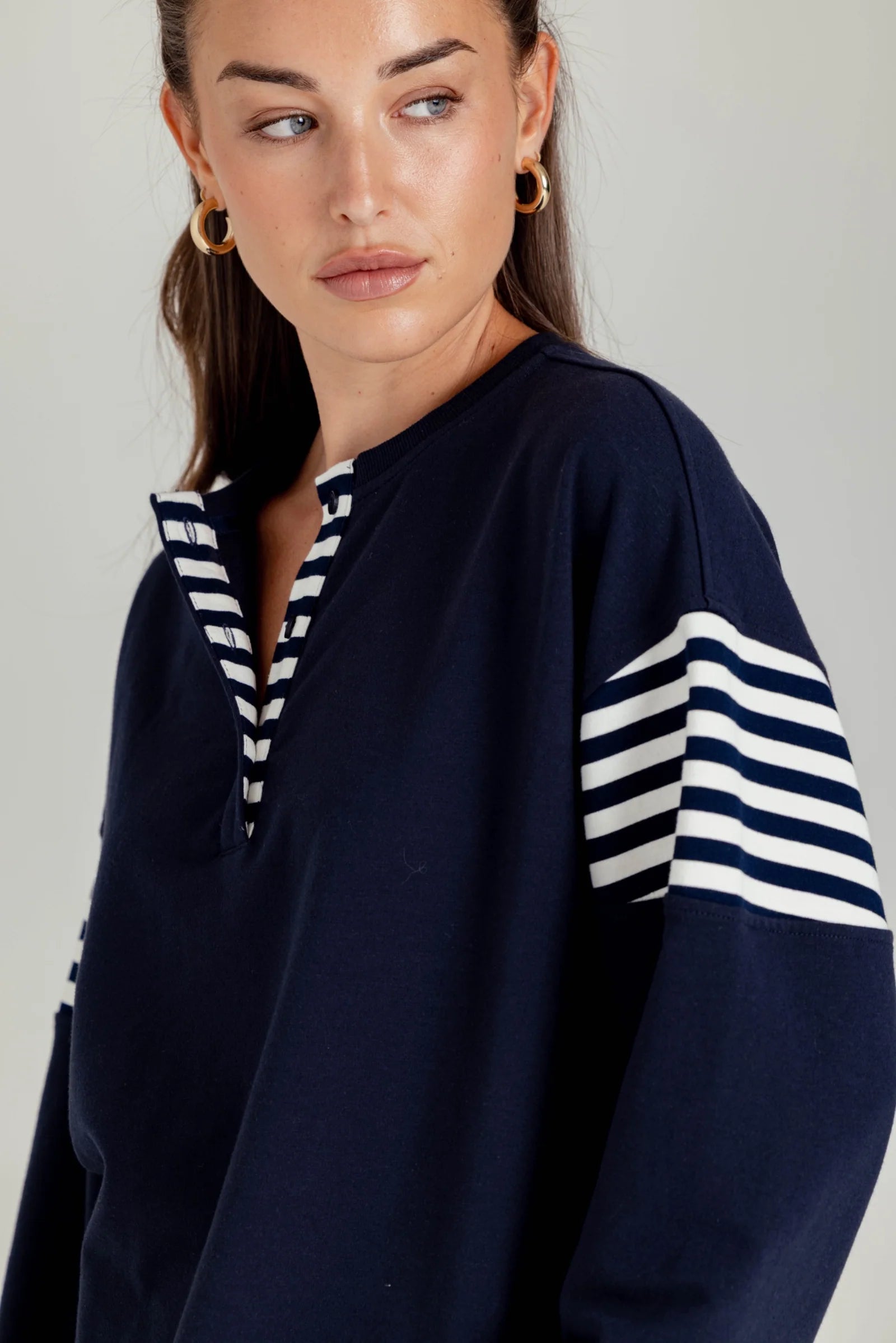 Woman wearing a navy blue sweater with white striped sleeves against a plain background