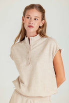 Woman wearing a beige sleeveless top against a plain background