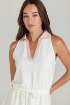 Woman wearing a white sleeveless top with pink trim against a plain background