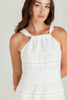 Woman wearing a white dress with lace details on a plain background