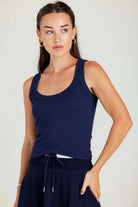 Woman wearing a navy blue tank top and dark pants against a plain background