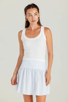 Woman wearing a white tank top and light blue skirt on a plain background