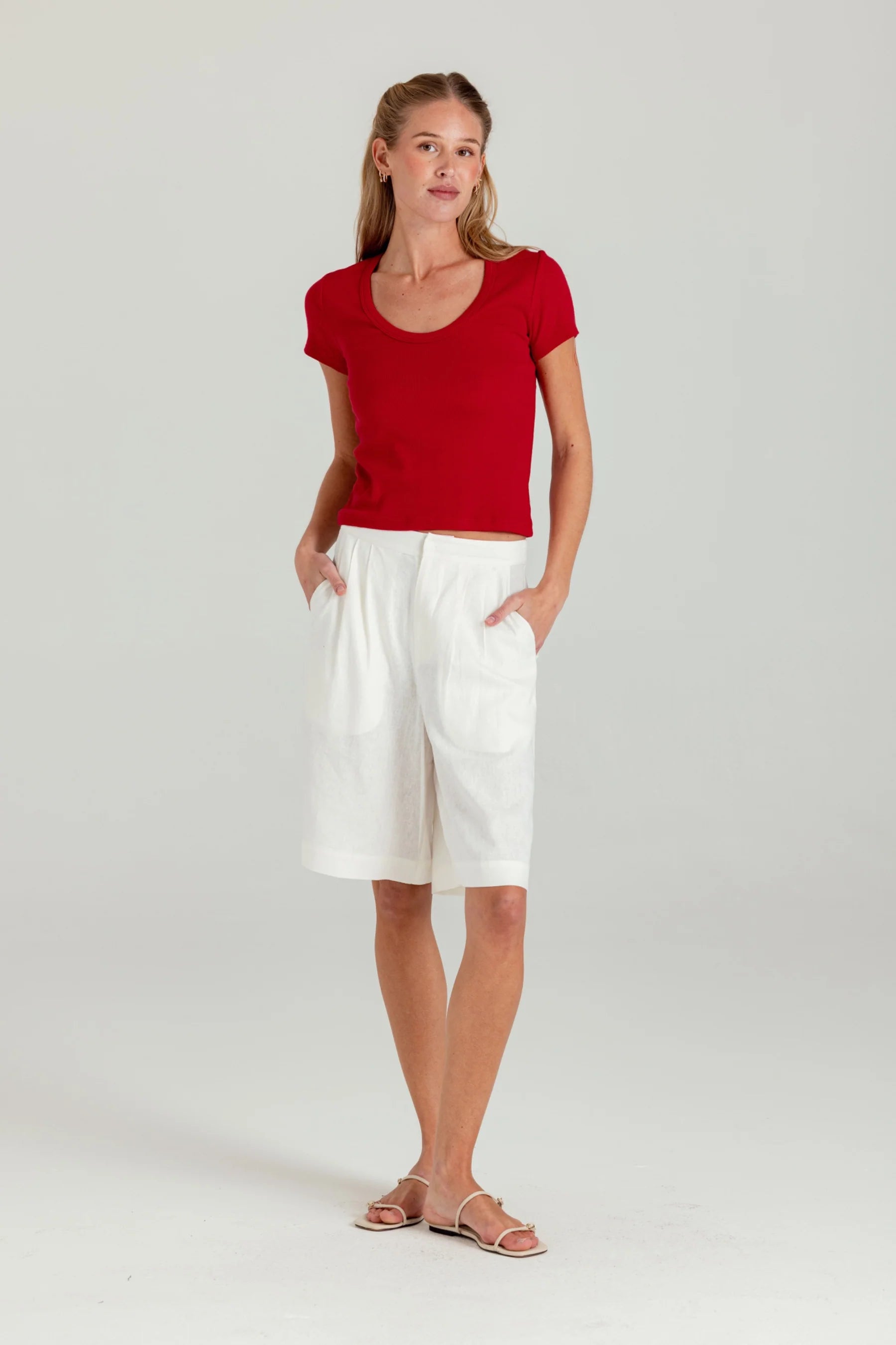 Woman wearing a red top and white shorts on a light gray background