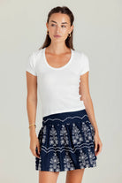 Woman wearing a white t-shirt and navy patterned skirt on a plain background