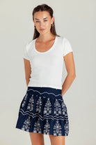 Woman wearing a white t-shirt and navy skirt with white patterns on a plain background