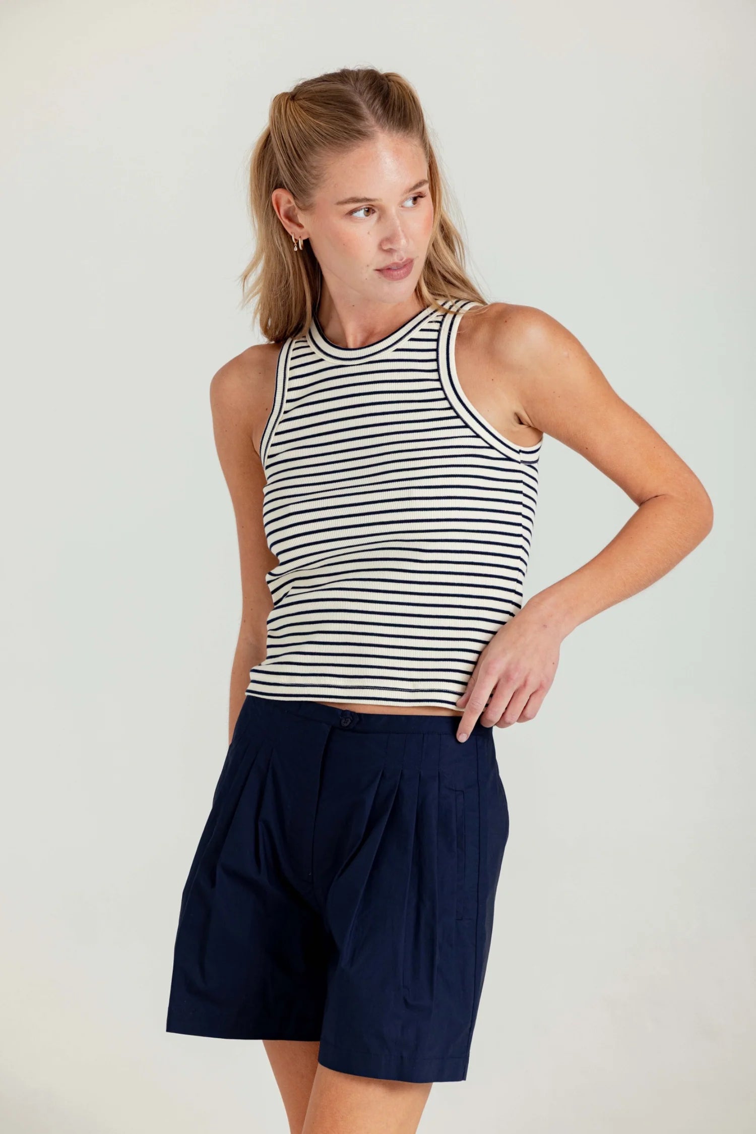 Woman wearing a striped tank top and navy shorts on a plain background