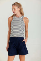 Woman wearing a striped tank top and navy shorts on a white background