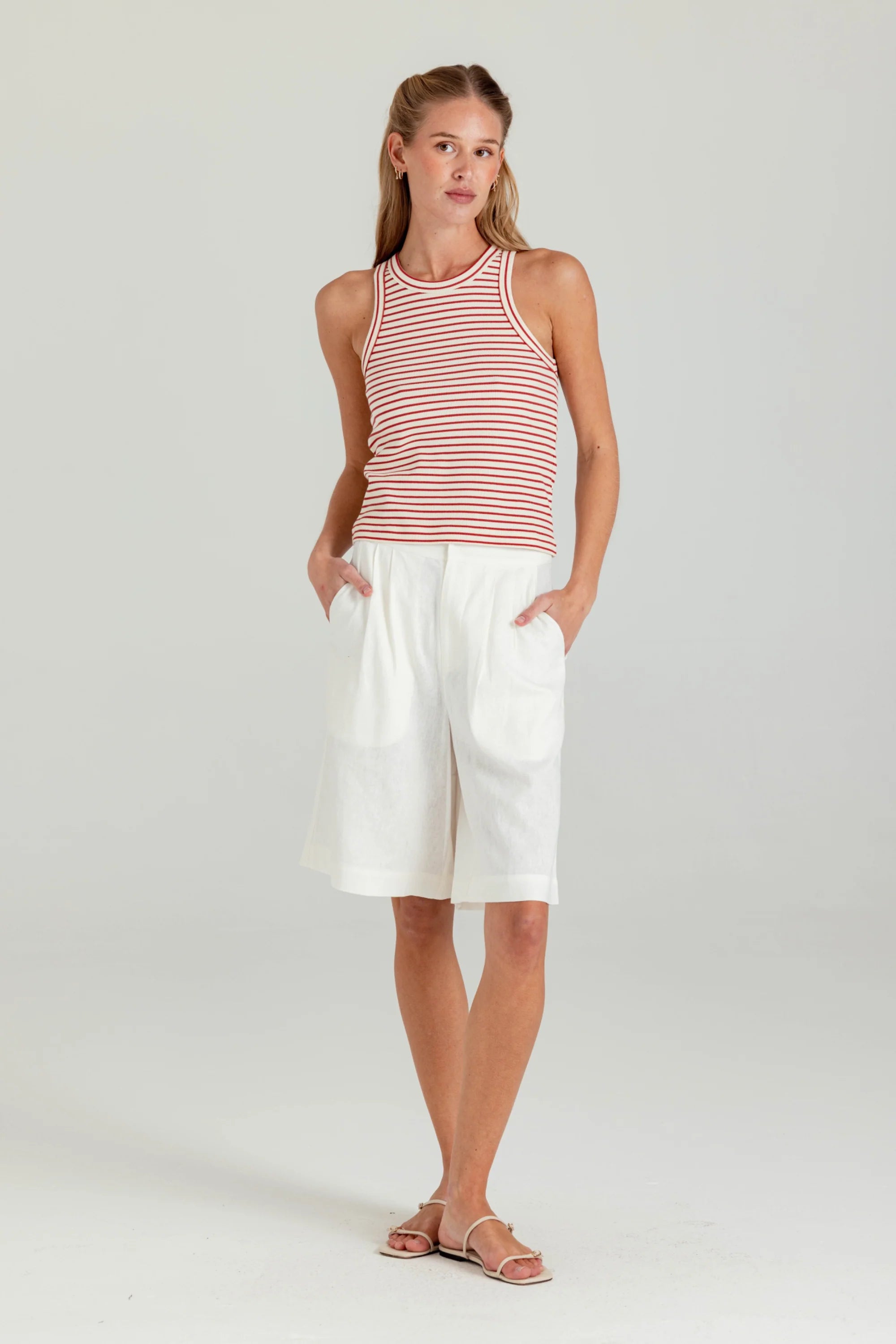 Woman wearing a striped tank top and white shorts on a plain background