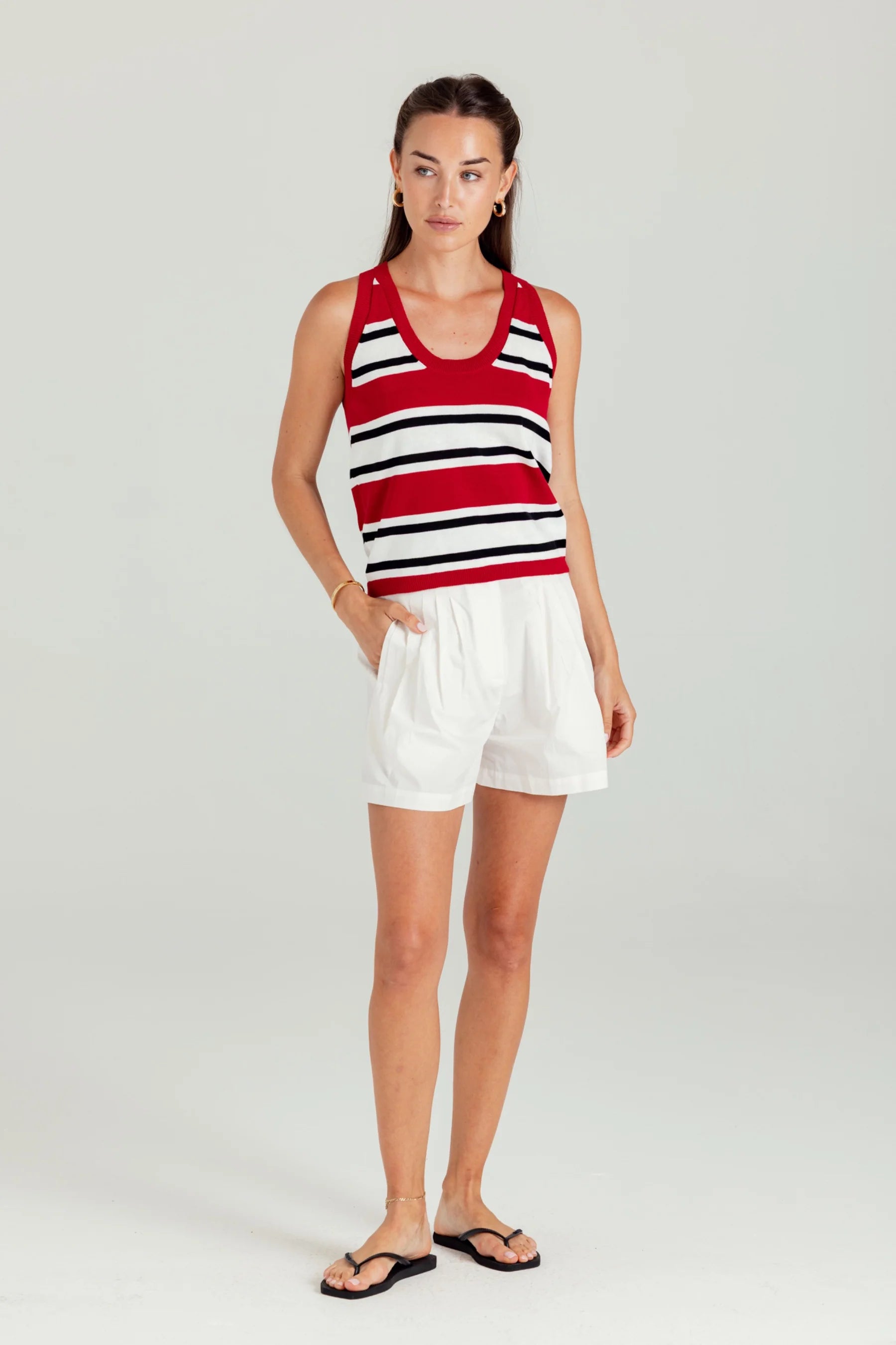 Woman wearing a red and white striped tank top and white shorts on a plain background