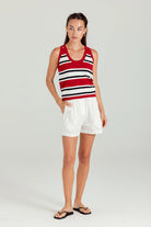 Woman wearing a red and white striped tank top and white shorts on a plain background