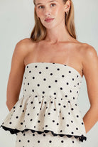 Woman wearing a strapless polka dot dress against a plain background