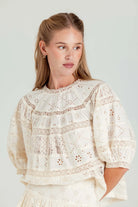 Woman wearing a cream-colored lace blouse against a plain background