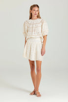 Woman wearing a cream-colored outfit with a top and skirt on a white background
