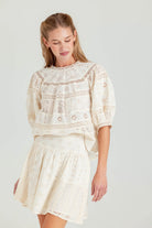 Woman wearing a cream-colored lace dress against a plain background