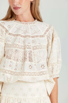 Close-up of a person wearing a white lace blouse against a plain background