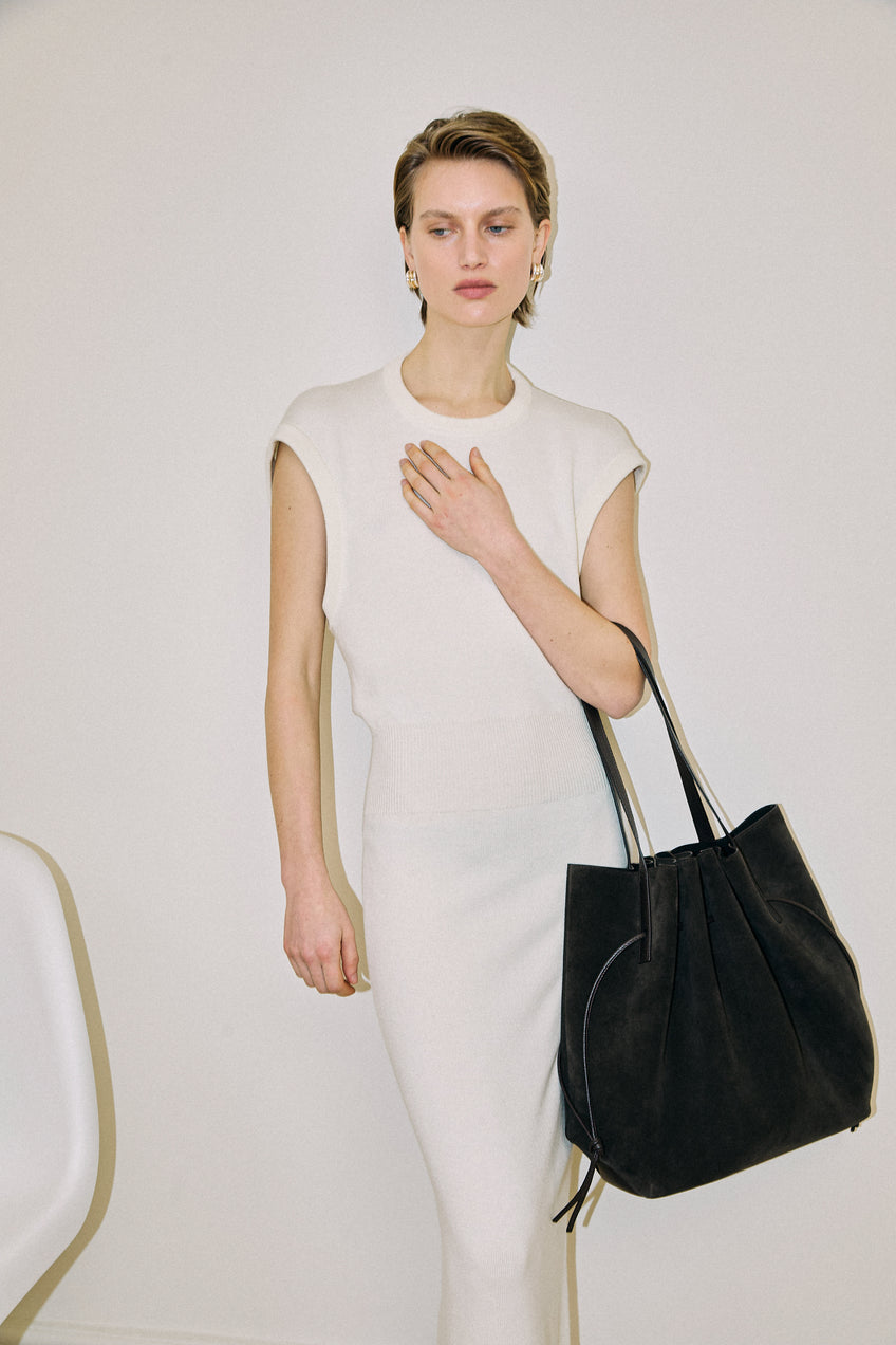 Woman holding a black handbag against a plain background