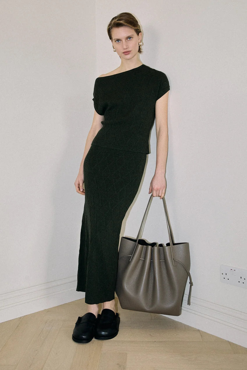 Woman in a black dress holding a gray handbag against a plain background