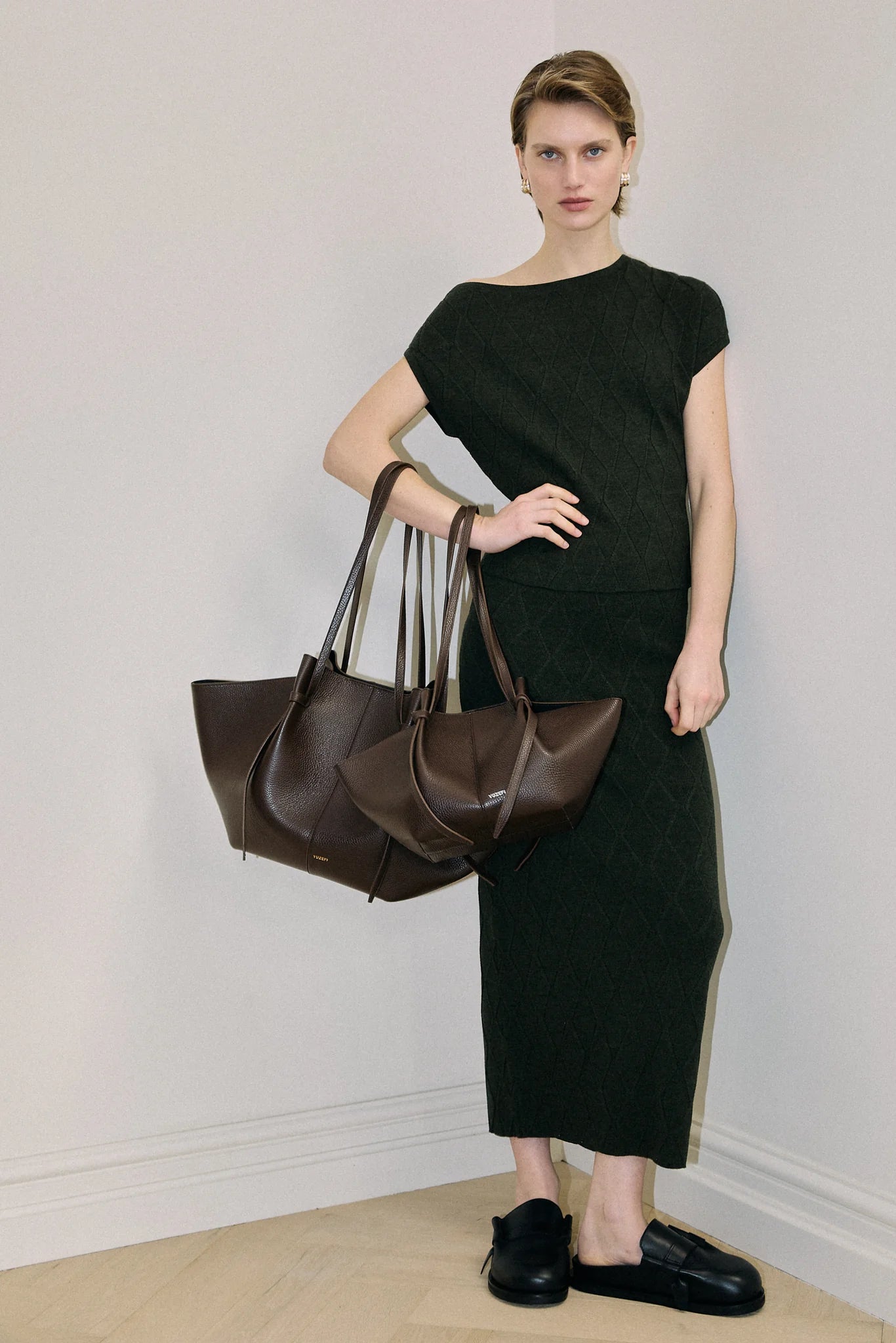 Woman holding two brown handbags against a plain background