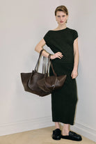 Woman holding two brown handbags against a plain background