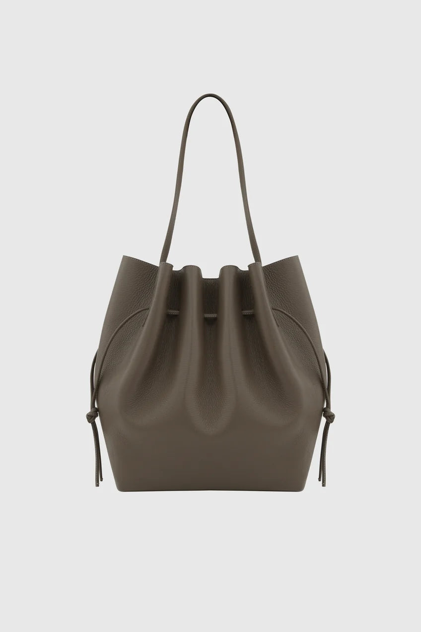 A dark taupe leather bucket bag with a drawstring closure and a single shoulder strap, shown against a light gray background.