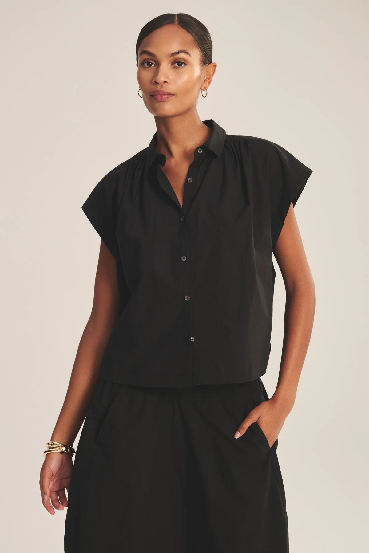 Woman wearing a black sleeveless blouse with a plain background