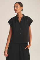 Woman wearing a black sleeveless blouse against a plain background
